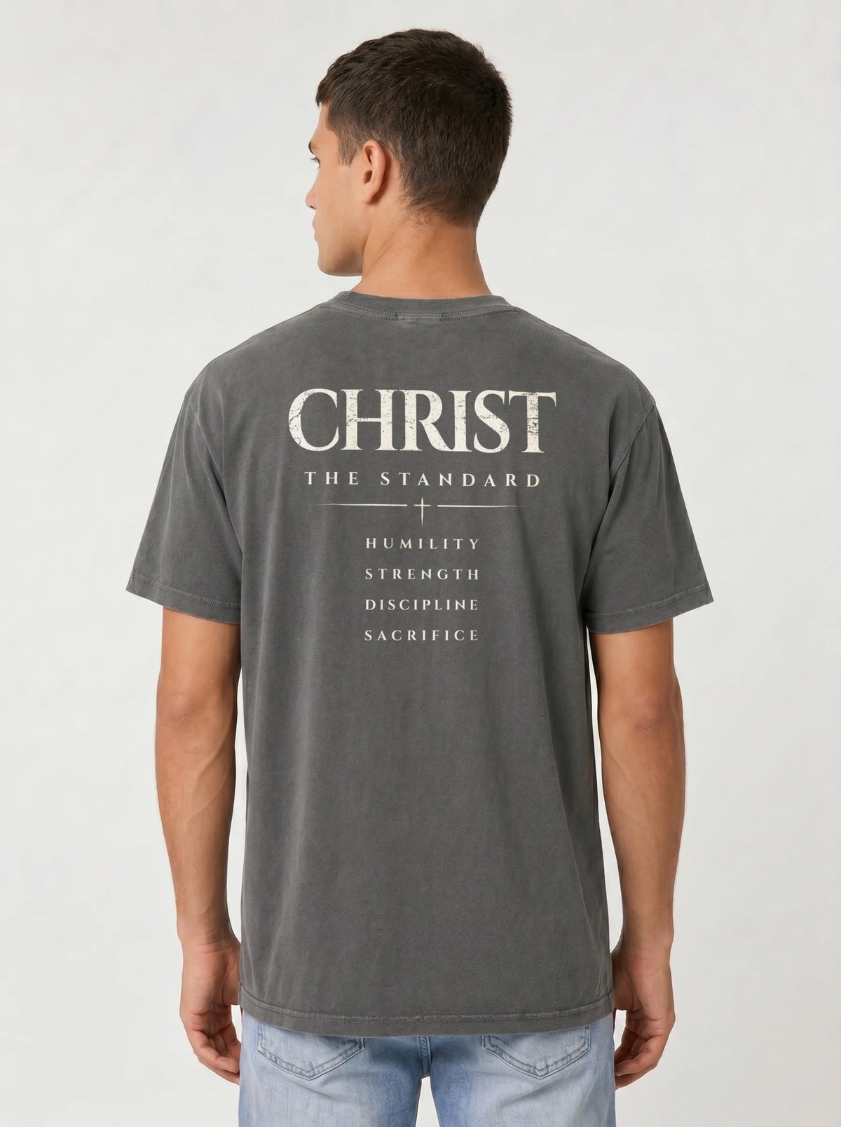 Person wearing a gray T-shirt with back text reading “Christ The Standard,” followed by “Humility, Strength, Discipline, Sacrifice” and a small cross.