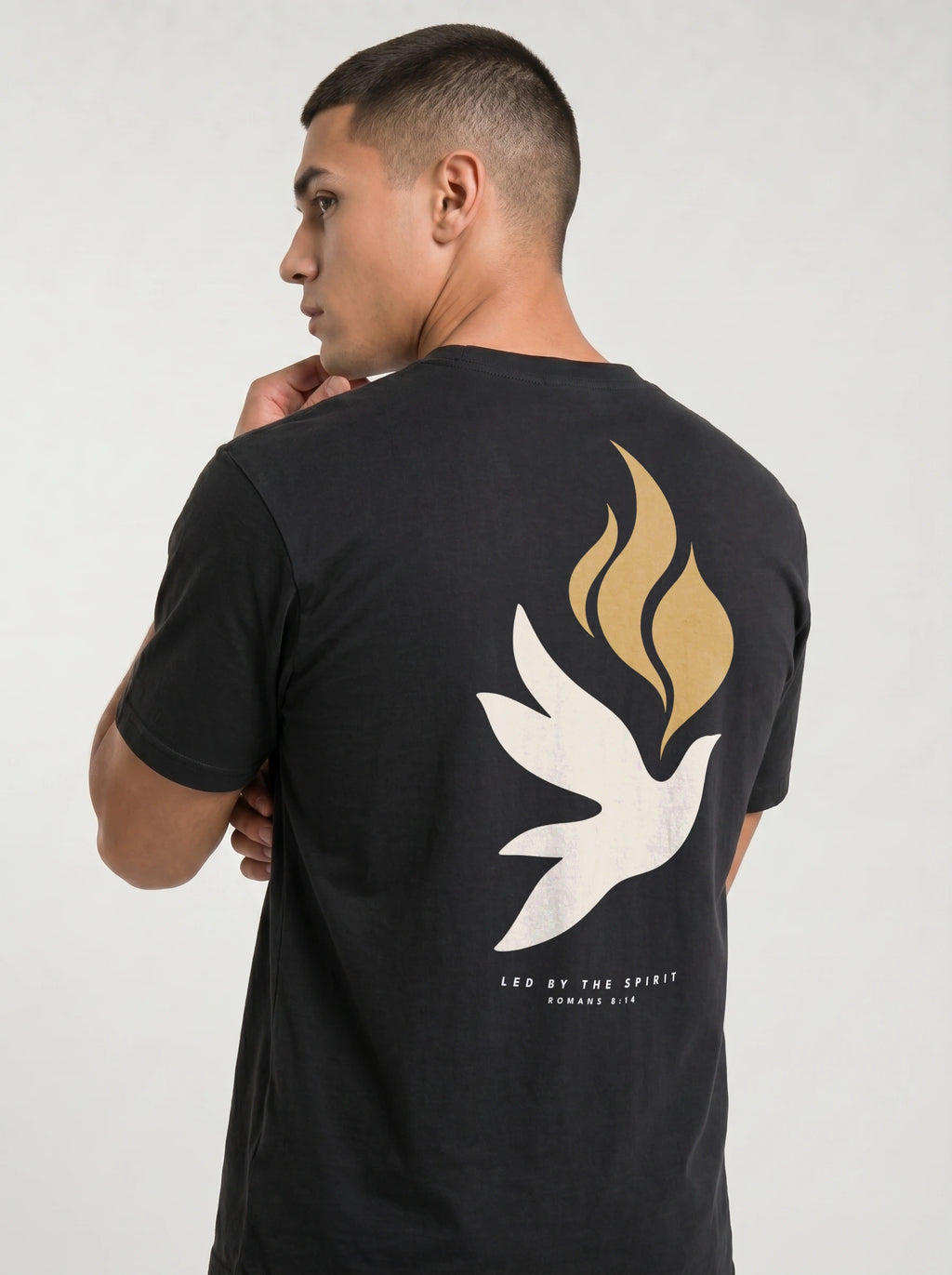 Person wearing a black T-shirt with a large white dove, gold flames, and “LED BY THE SPIRIT ROMANS 8:14” on the back.