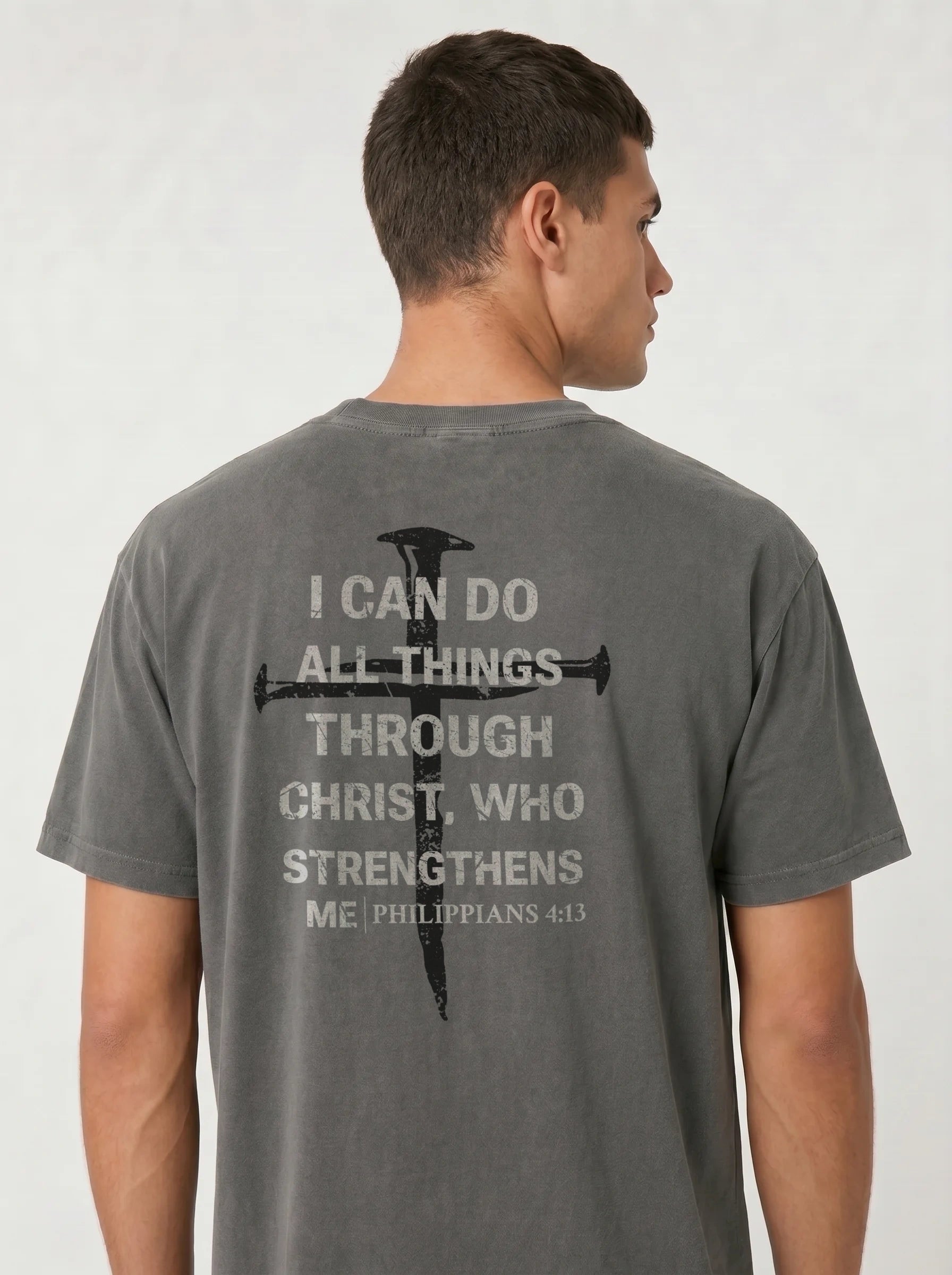 A man wearing a dark gray t-shirt, viewed from the back. The shirt features a black graphic of a cross with a sword and white text that reads 'I CAN DO ALL THINGS THROUGH CHRIST, WHO STRENGTHENS ME PHILIPPIANS 4:13'.