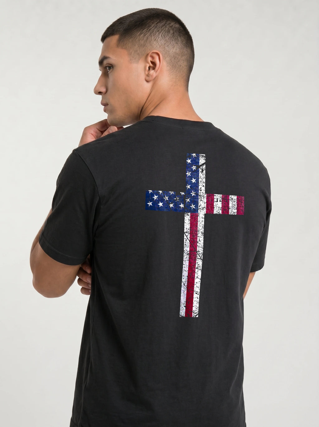 A man wearing a black t-shirt, viewed from the back. The shirt features a large distressed cross graphic on the back, filled with the American flag pattern of blue stars and red and white stripes.