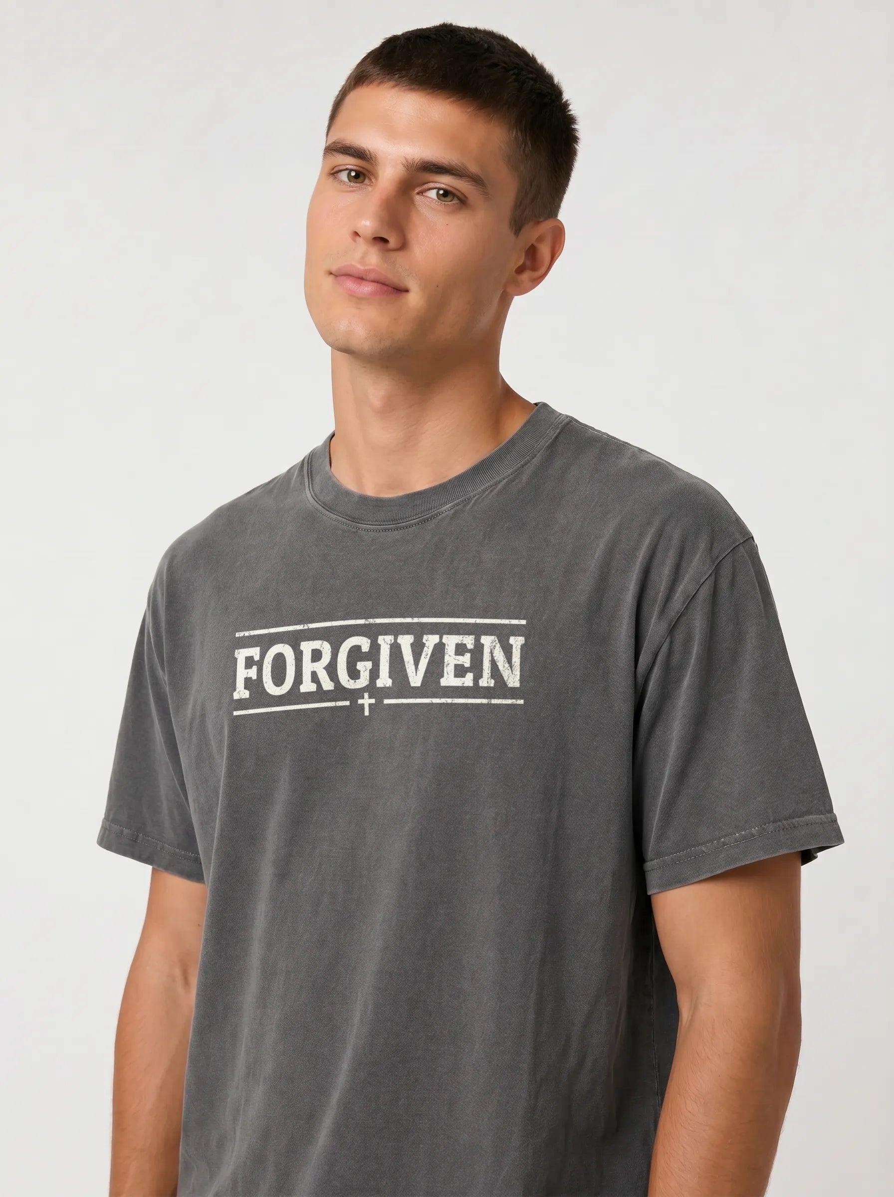 A man wearing a dark gray mineral-wash t-shirt with 'FORGIVEN' printed in white across the chest, photographed against a light gray studio background.