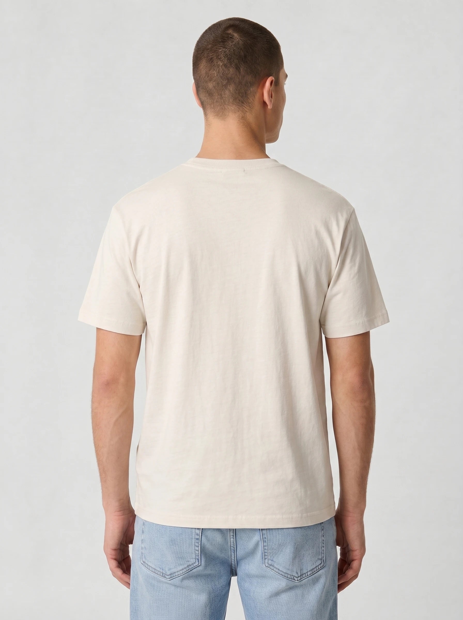 A man viewed from the back wearing a plain cream-colored short-sleeve t-shirt and light blue jeans, set against a neutral light gray background.