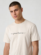 Close view of a cream T-shirt with black script reading “Jesus Saves,” with a cross incorporated into the lettering.
