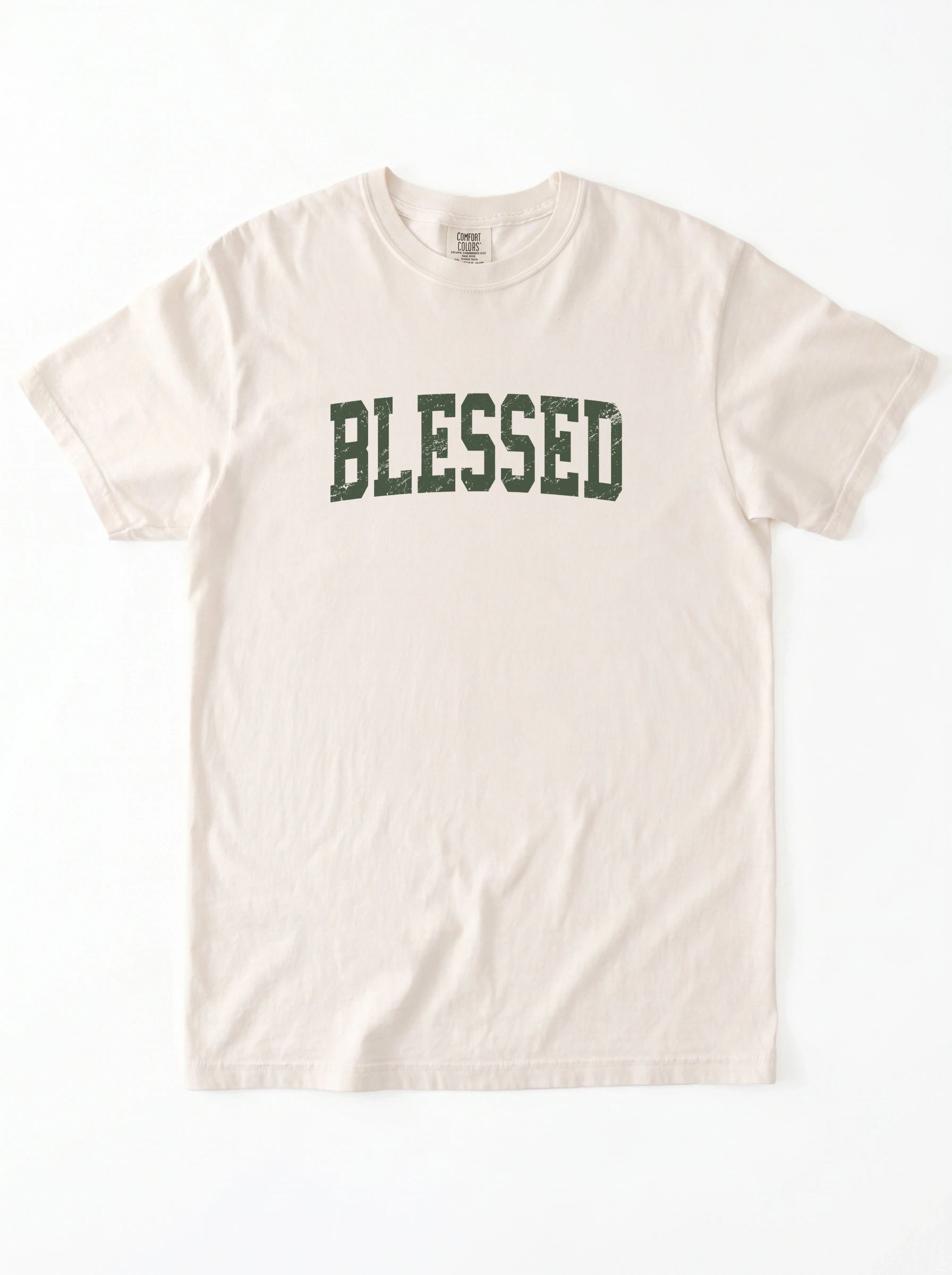 A light beige crewneck t-shirt with the word 'BLESSED' printed across the chest in a dark green collegiate-style font, laid flat against a white background.