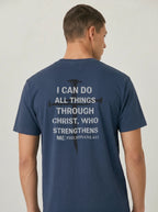 A man wearing a navy blue t-shirt, viewed from the back. The shirt features a white printed text graphic that reads 'I CAN DO ALL THINGS THROUGH CHRIST, WHO STRENGTHENS ME PHILIPPIANS 4:13' overlaid on a black cross silhouette.