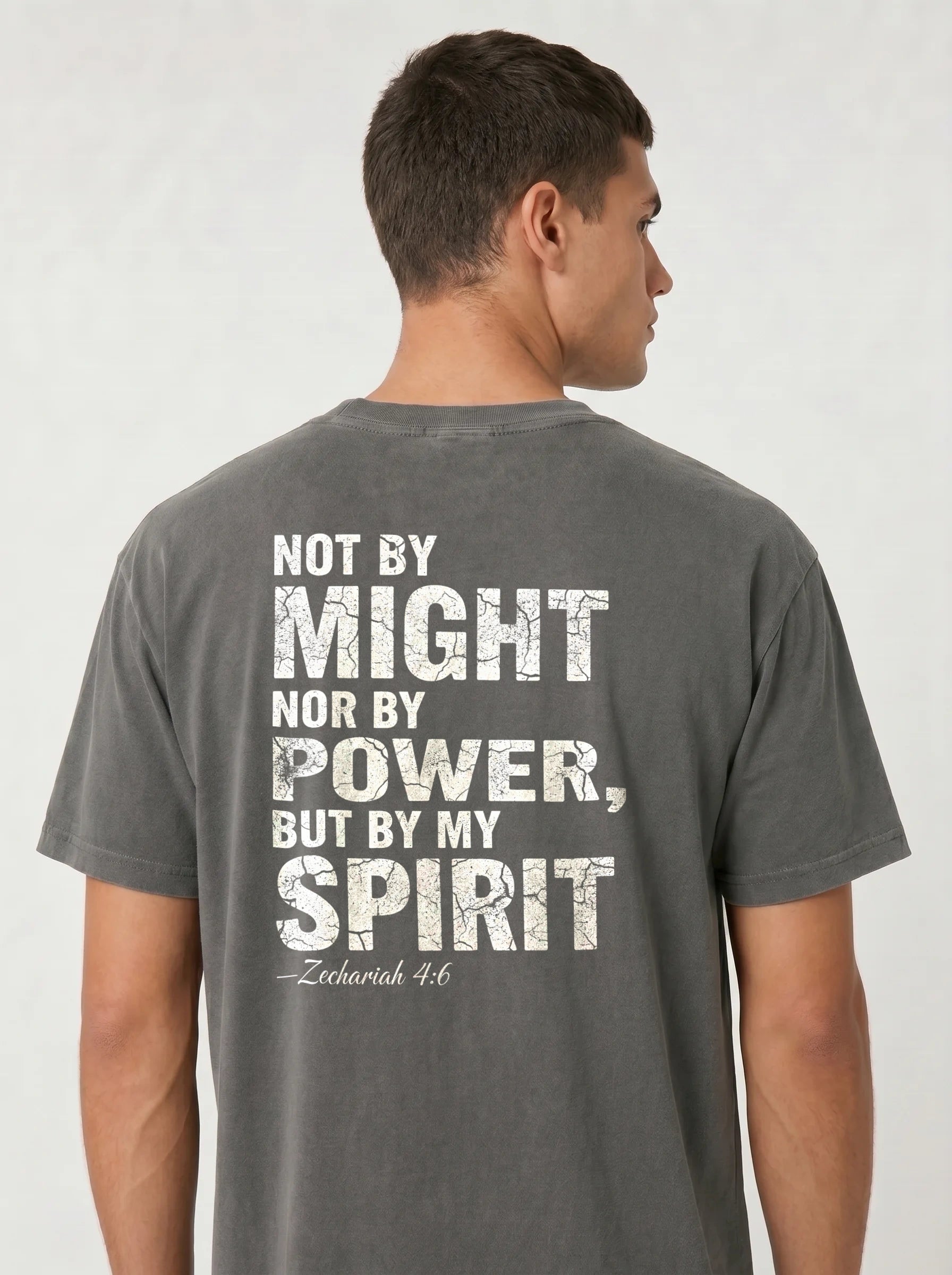 A man viewed from the back wearing a dark gray t-shirt with a distressed white typographic print that reads 'NOT BY MIGHT NOR BY POWER, BUT BY MY SPIRIT - Zechariah 4:6'.