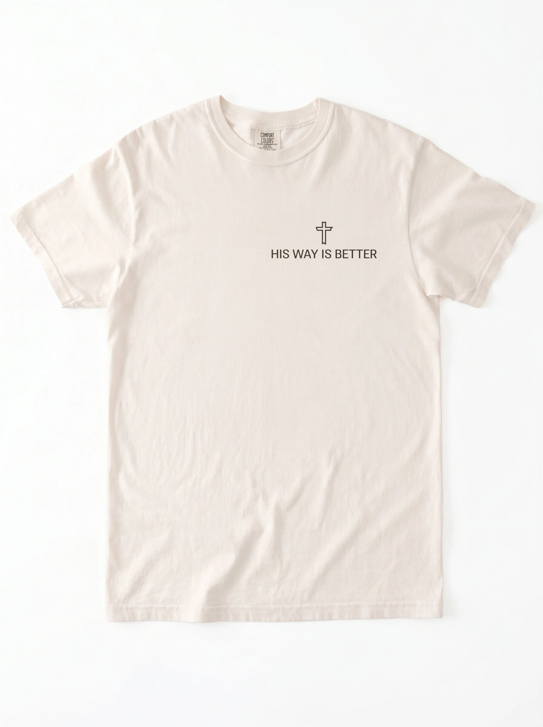 A light beige crewneck t-shirt with a small black graphic on the left chest featuring a cross and the text 'HIS WAY IS BETTER'.