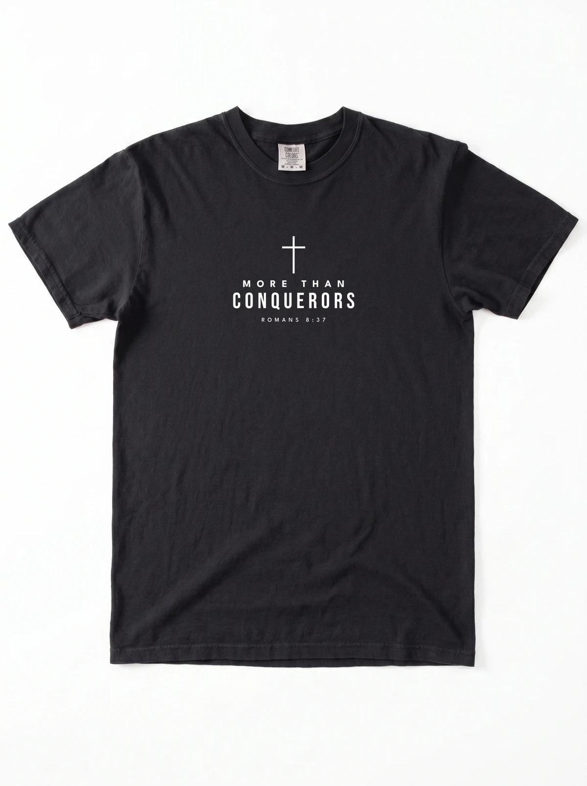 Black T-shirt laid flat with a white cross and the text “More Than Conquerors” and “Romans 8:37.”