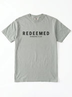 A light gray short-sleeve crewneck t-shirt with 'REDEEMED ROMANS 3:24' printed in black across the chest, displayed flat against a white background.