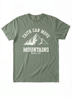 An olive green short-sleeve t-shirt with a white graphic print on the front featuring a mountain illustration and the text 'FAITH CAN MOVE MOUNTAINS Matthew 17:20'.