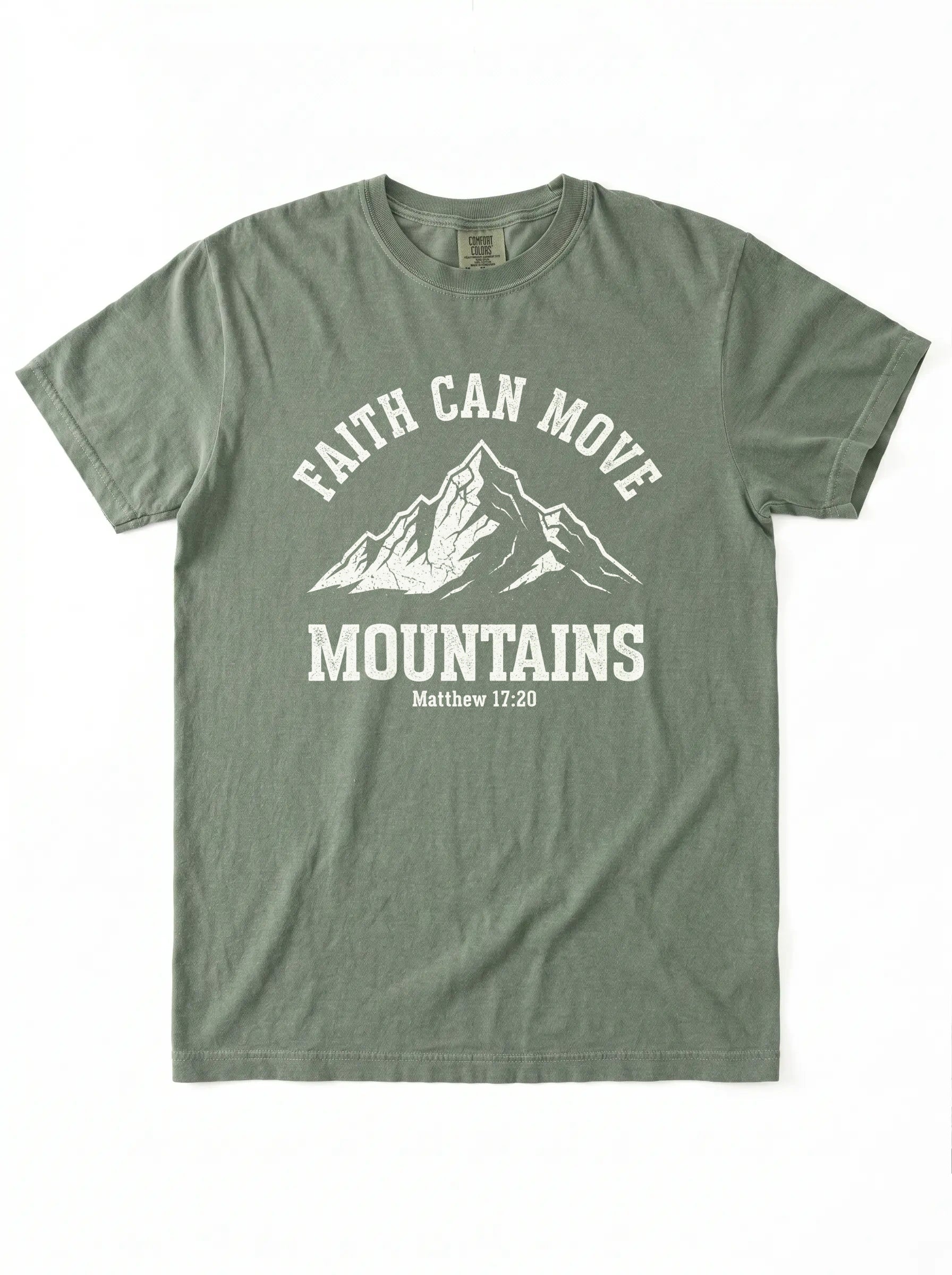 An olive green short-sleeve t-shirt with a white graphic print on the front featuring a mountain illustration and the text 'FAITH CAN MOVE MOUNTAINS Matthew 17:20'.
