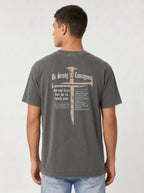 A man wearing a dark gray washed t-shirt from the back, featuring a large graphic print of a cross with a nail through it and the text 'Be Strong & Courageous' and 'do not fear for he is with you'.