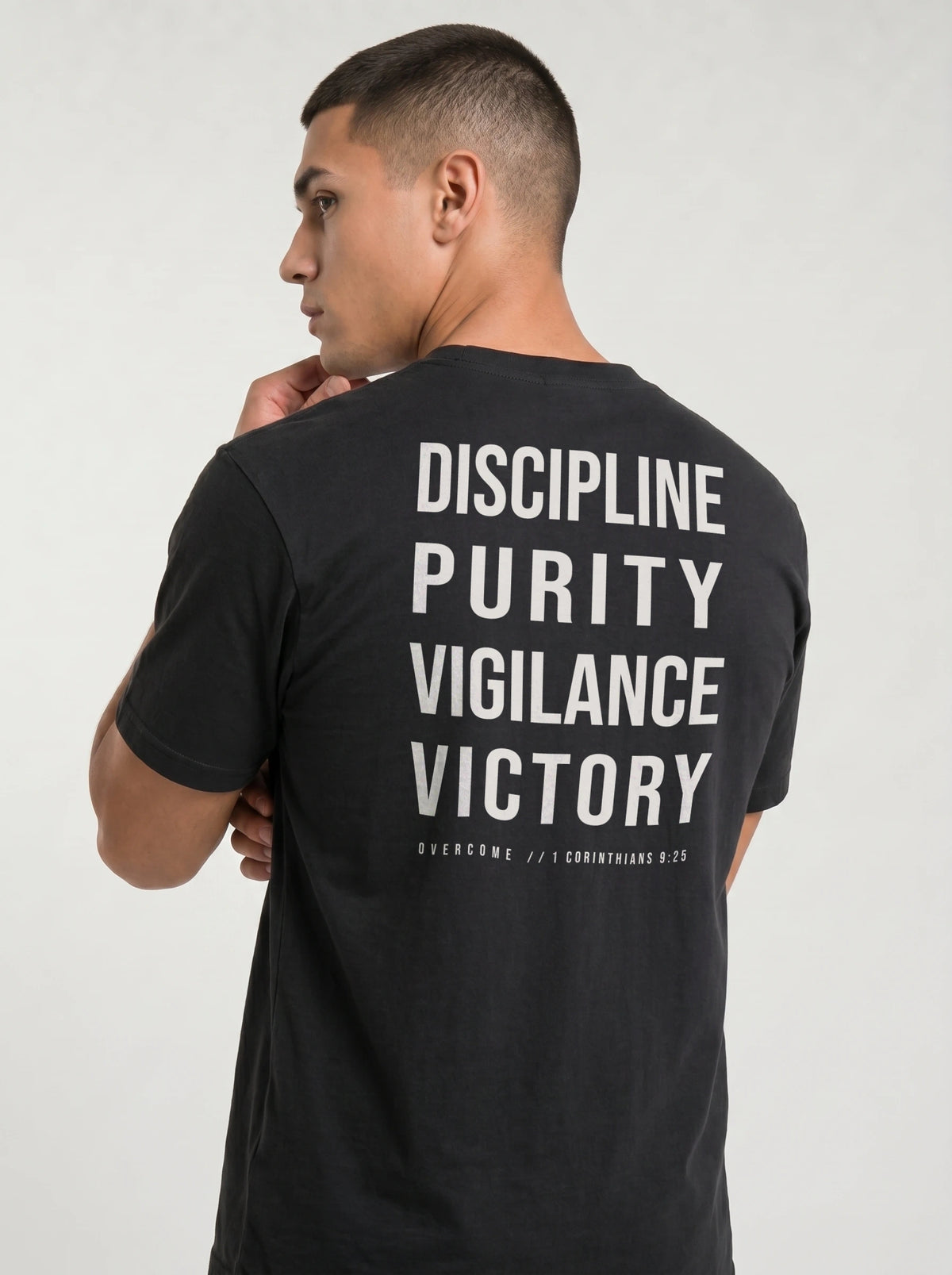 Angled back view of a person in a black T-shirt reading “Discipline Purity Vigilance Victory” and “Overcome // 1 Corinthians 9:25.”