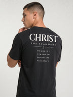 Angled back view of a person in a black T-shirt reading “Christ The Standard,” with a cross and “Humility, Strength, Discipline, Sacrifice.”