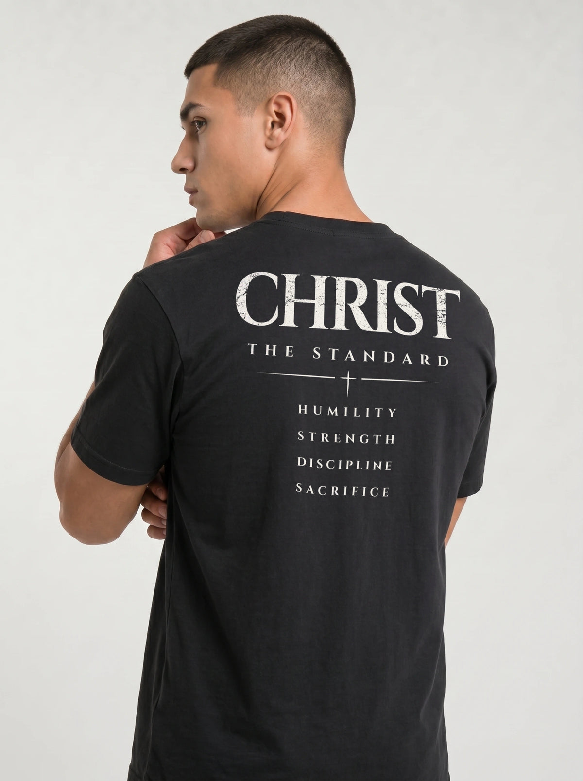 Angled back view of a person in a black T-shirt reading “Christ The Standard,” with a cross and “Humility, Strength, Discipline, Sacrifice.”