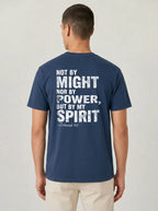 A man viewed from the back wearing a navy blue t-shirt with a distressed white graphic text that reads 'NOT BY MIGHT NOR BY POWER, BUT BY MY SPIRIT -Zechariah 4:6'.