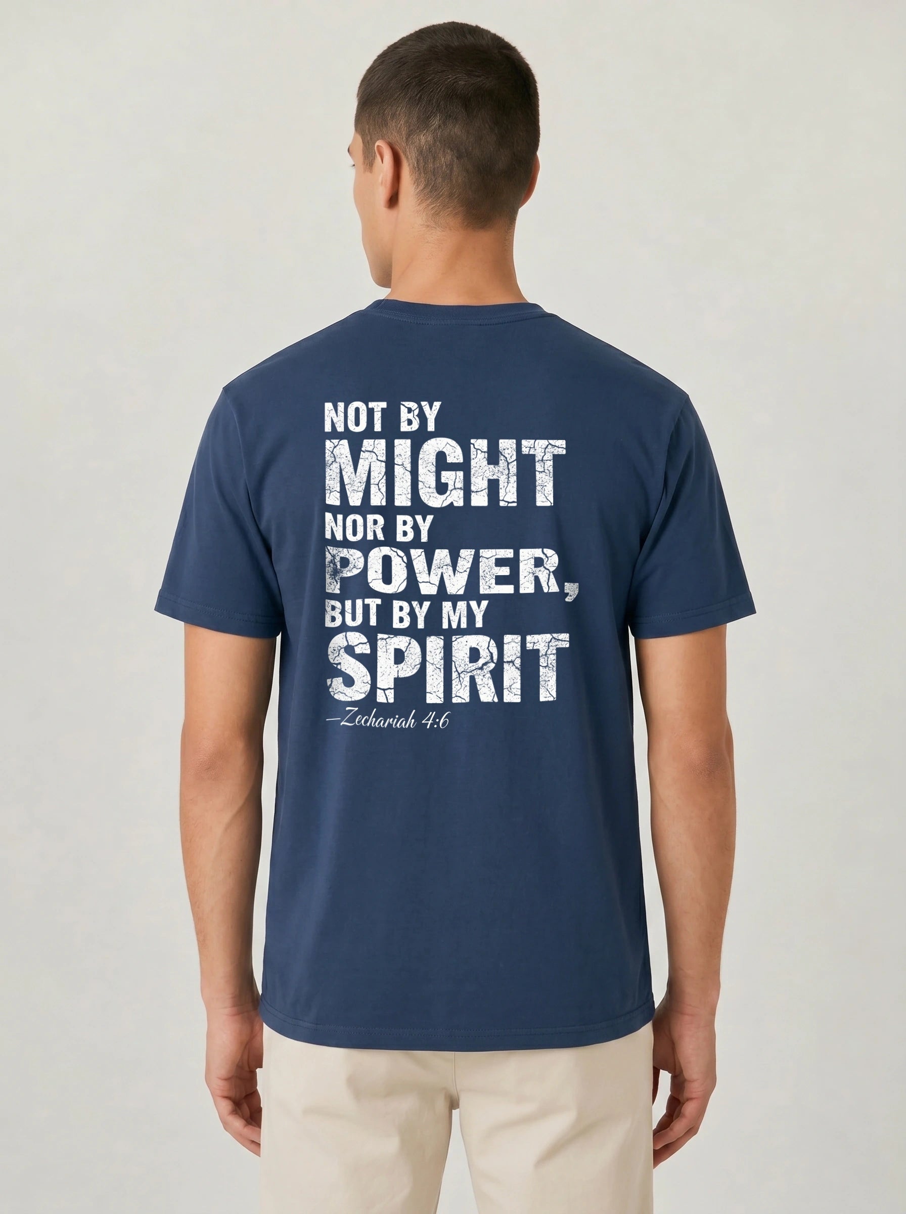 A man viewed from the back wearing a navy blue t-shirt with a distressed white graphic text that reads 'NOT BY MIGHT NOR BY POWER, BUT BY MY SPIRIT -Zechariah 4:6'.