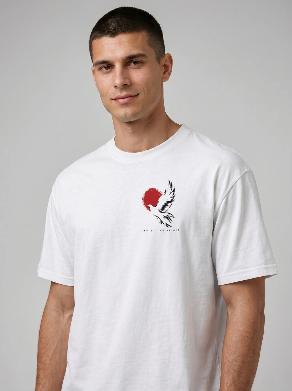 Person wearing a white T-shirt with a black-and-white flying bird against a red circle and “LED BY THE SPIRIT” on the chest.