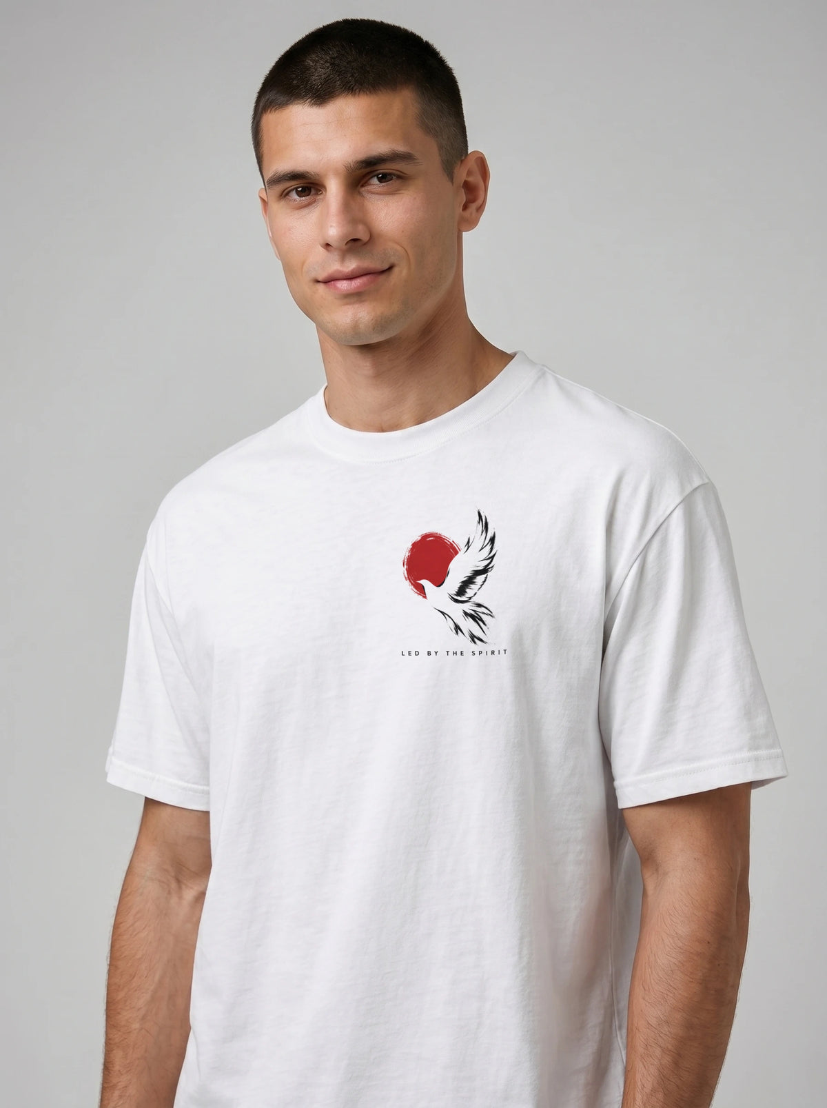 Person wearing a white T-shirt with a black-and-white flying bird against a red circle and “LED BY THE SPIRIT” on the chest.