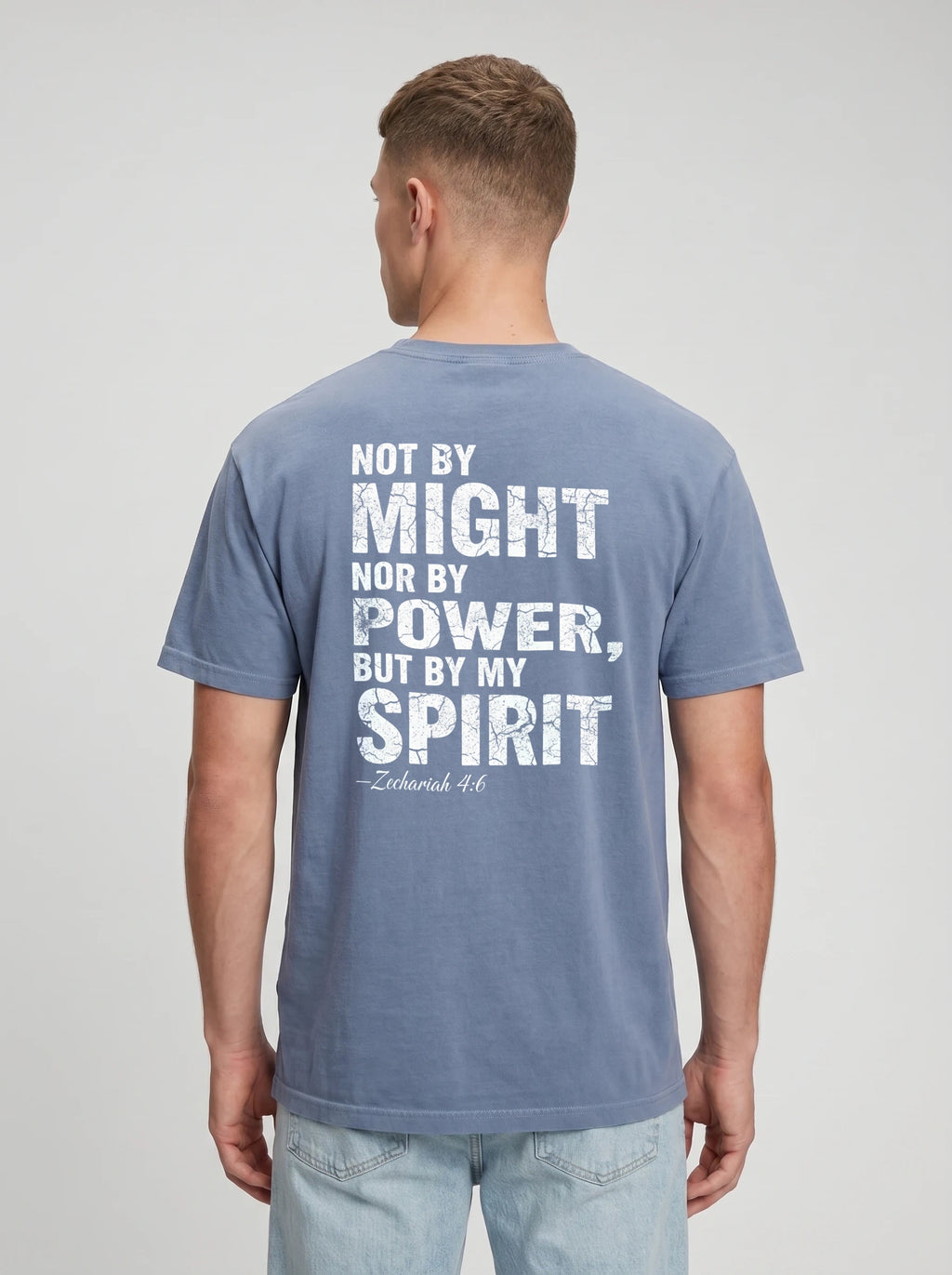 A man viewed from the back wearing a slate blue t-shirt with a distressed white graphic quote on the back reading 'NOT BY MIGHT NOR BY POWER, BUT BY MY SPIRIT -Zechariah 4:6'.