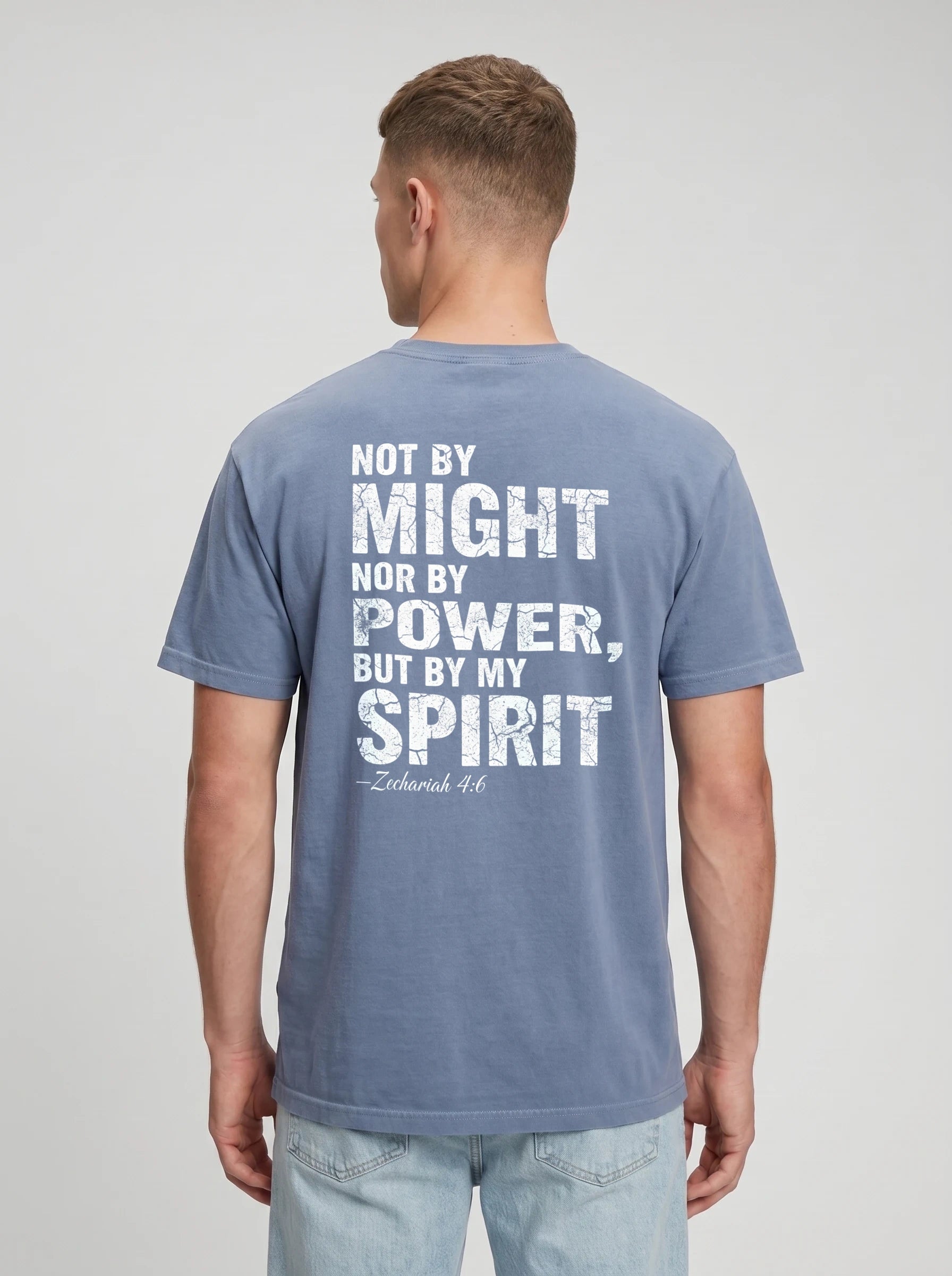 A man viewed from the back wearing a slate blue t-shirt with a distressed white graphic quote on the back reading 'NOT BY MIGHT NOR BY POWER, BUT BY MY SPIRIT -Zechariah 4:6'.