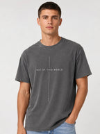 Person wearing a faded gray T-shirt with thin white lines framing the text “Not of This World” and “John 17:16.”