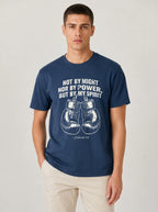 A man wearing a navy blue t-shirt with a white graphic print of boxing gloves and the quote 'NOT BY MIGHT NOR BY POWER, BUT BY MY SPIRIT' on a light gray studio background.