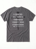 A dark gray crewneck t-shirt shown from the back, featuring a distressed white text graphic of the biblical quote 'I CAN DO ALL THINGS THROUGH CHRIST, WHO STRENGTHENS ME' alongside a black cross design.