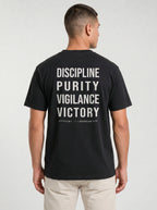 Person wearing a black T-shirt with large back text reading “Discipline Purity Vigilance Victory” and “Overcome // 1 Corinthians 9:25.”