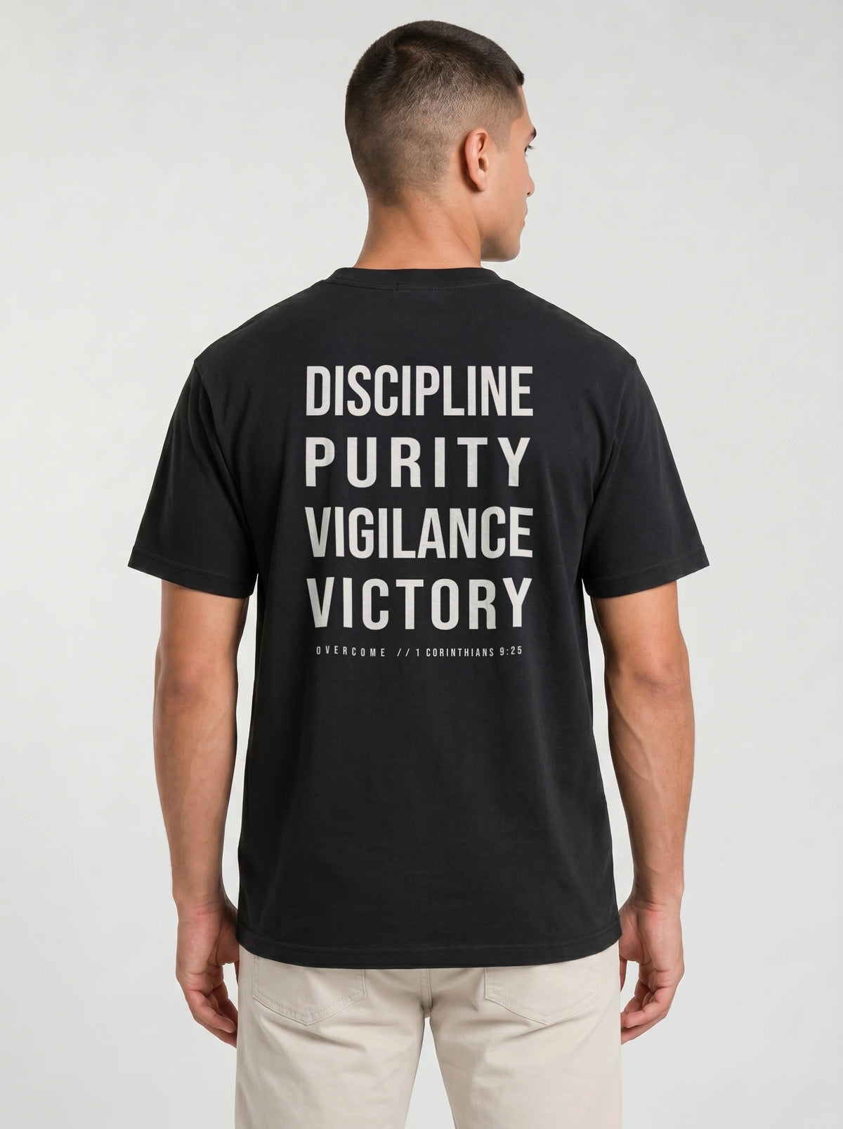 Person wearing a black T-shirt with large back text reading “Discipline Purity Vigilance Victory” and “Overcome // 1 Corinthians 9:25.”