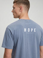A man shown from the back wearing a heathered blue-gray t-shirt with 'HOPE ROMANS 15:13' printed in white on the back, against a light gray studio background.