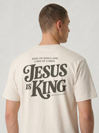 Person wearing a cream T-shirt with dark back text: “King of Kings and Lord of Lords. Jesus is King. Revelation 19:16.”