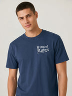 A man wearing a navy blue crewneck t-shirt with 'King of Kings' printed in white Gothic lettering on the chest, photographed against a neutral light gray background.