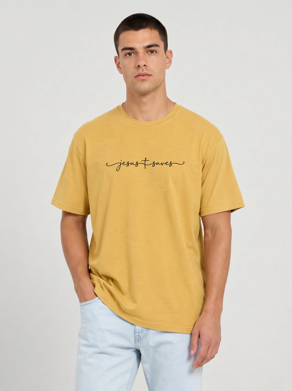 Person wearing a mustard yellow T-shirt with black script reading “Jesus Saves,” with a cross incorporated into the lettering.