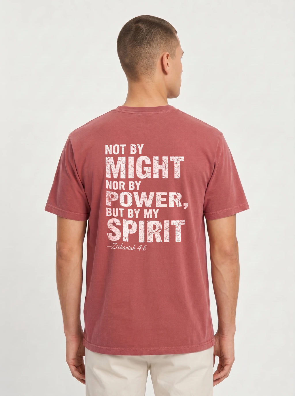 A man viewed from the back wearing a faded dusty rose t-shirt with a distressed white typographic print on the back that reads 'NOT BY MIGHT NOR BY POWER, BUT BY MY SPIRIT -Zechariah 4:6'.