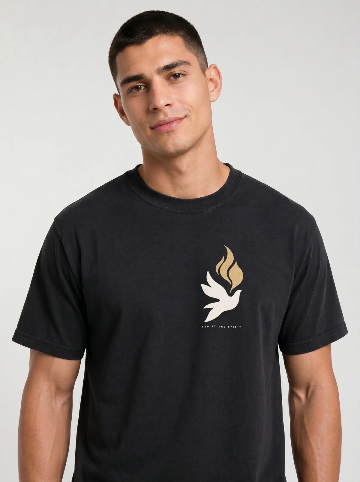 Person wearing a black T-shirt with a small white dove, gold flames, and “LED BY THE SPIRIT” on the chest.