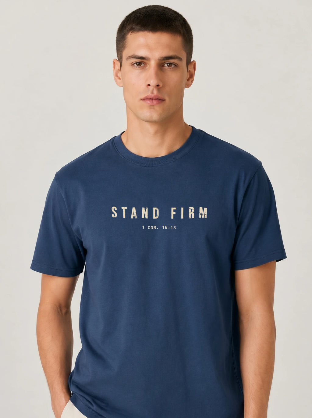 Person wearing a navy T-shirt with distressed beige text reading “Stand Firm” and “1 Cor. 16:13.”