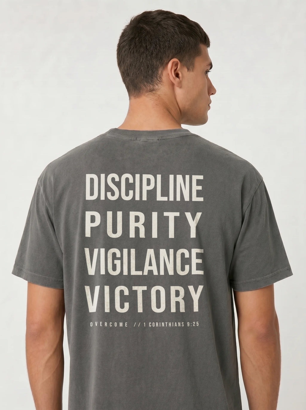 Person wearing a gray T-shirt with large back text reading “Discipline Purity Vigilance Victory” and “Overcome // 1 Corinthians 9:25.”