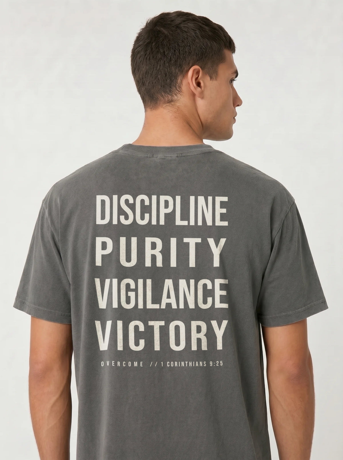 Person wearing a gray T-shirt with large back text reading “Discipline Purity Vigilance Victory” and “Overcome // 1 Corinthians 9:25.”