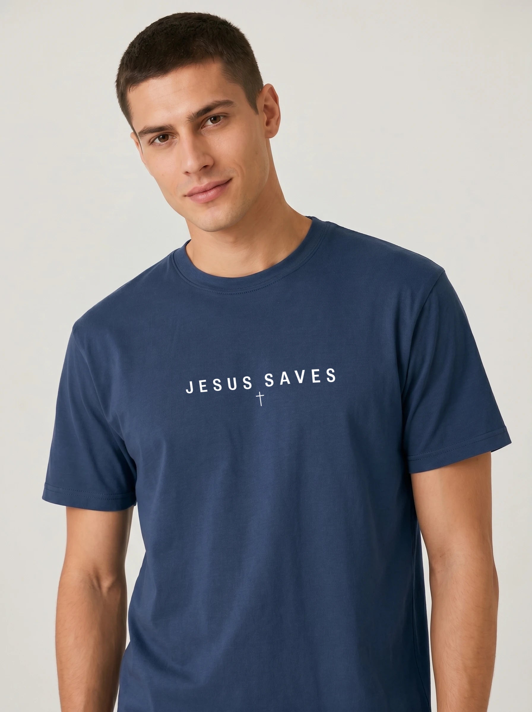 A man wearing a navy blue crewneck t-shirt with the white printed text 'JESUS SAVES' printed in white across the chest, photographed against a light gray studio background.