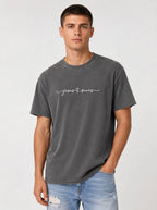 Person wearing a charcoal T-shirt with white script reading “Jesus Saves,” with a cross incorporated into the lettering.
