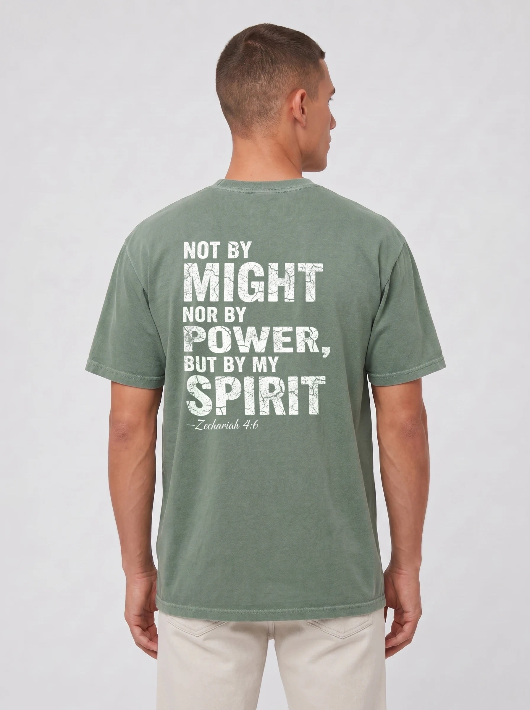 A man viewed from the back wearing a sage green t-shirt with a distressed white graphic text that reads 'NOT BY MIGHT NOR BY POWER, BUT BY MY SPIRIT -Zechariah 4:6'.