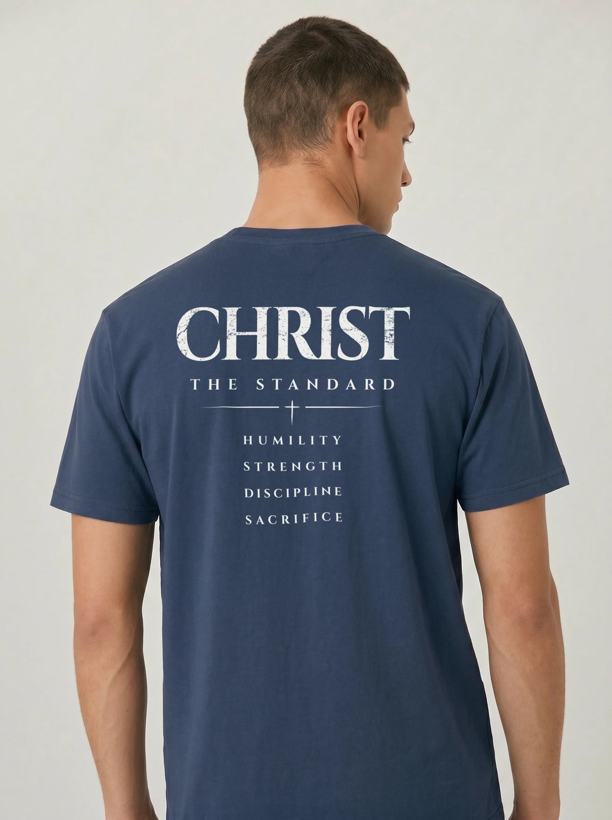 Person wearing a navy T-shirt with “Christ The Standard,” a small cross, and “Humility, Strength, Discipline, Sacrifice” on the back.