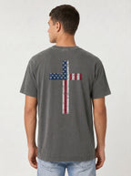 A man viewed from the back wearing a washed dark gray t-shirt with a distressed American flag cross graphic on the back, paired with light blue jeans, against a light gray studio background.