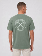 A man viewed from the back wearing a heathered sage green t-shirt with a large white circular graphic on the back with the text 'IRON SHARPENS IRON' and 'PROVERBS 27:17' surrounding an illustration of two crossed nails.