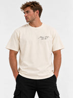 Person wearing a cream T-shirt with a small black script chest graphic reading “Man Of God.”