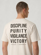 Person wearing a cream T-shirt with large back text reading “Discipline Purity Vigilance Victory” and “Overcome // 1 Corinthians 9:25.”