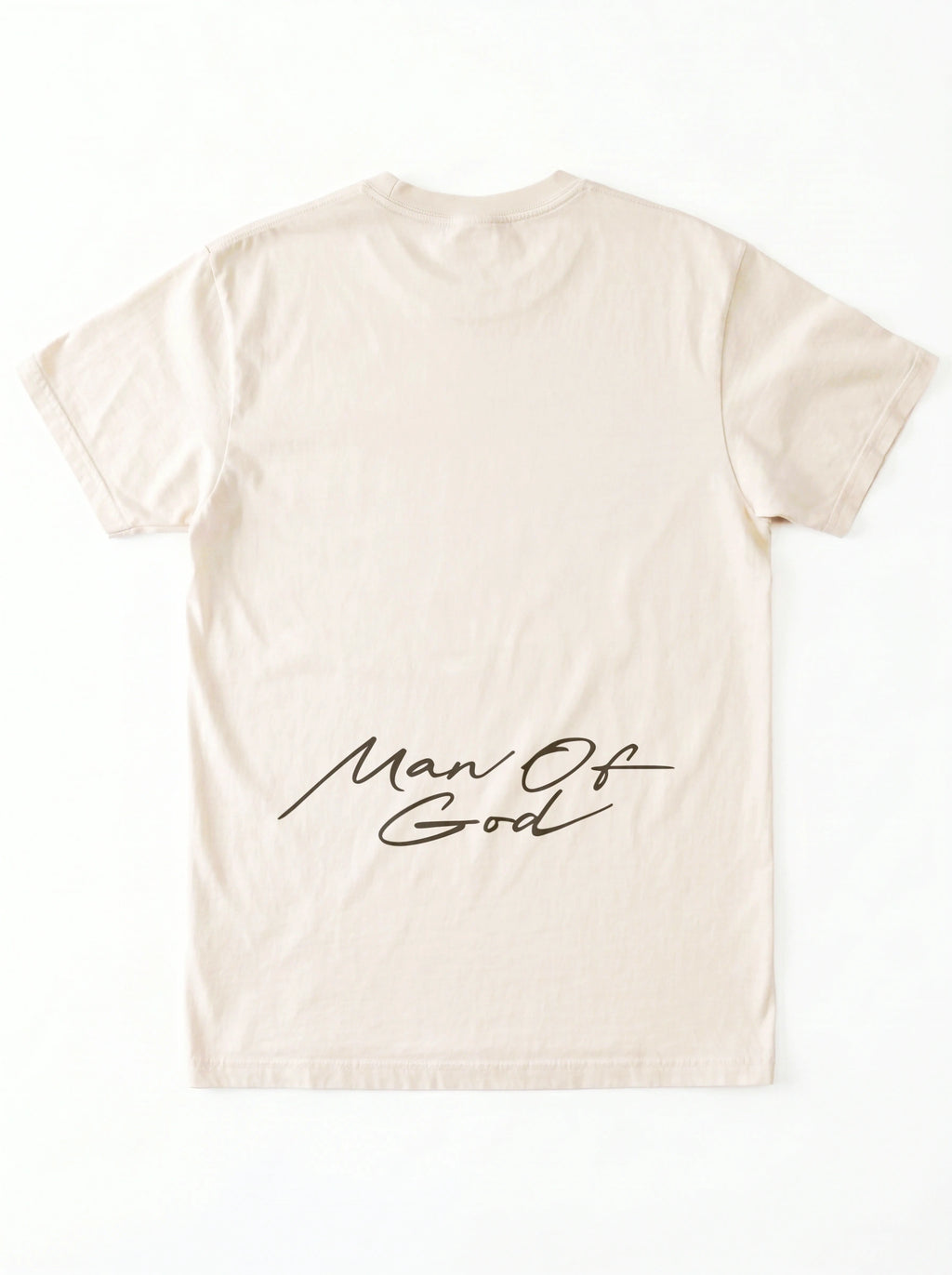 Back of a cream T-shirt laid flat with a large black script graphic across the lower back reading “Man Of God.”