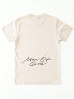 Back of a cream T-shirt laid flat with a large black script graphic across the lower back reading “Man Of God.”