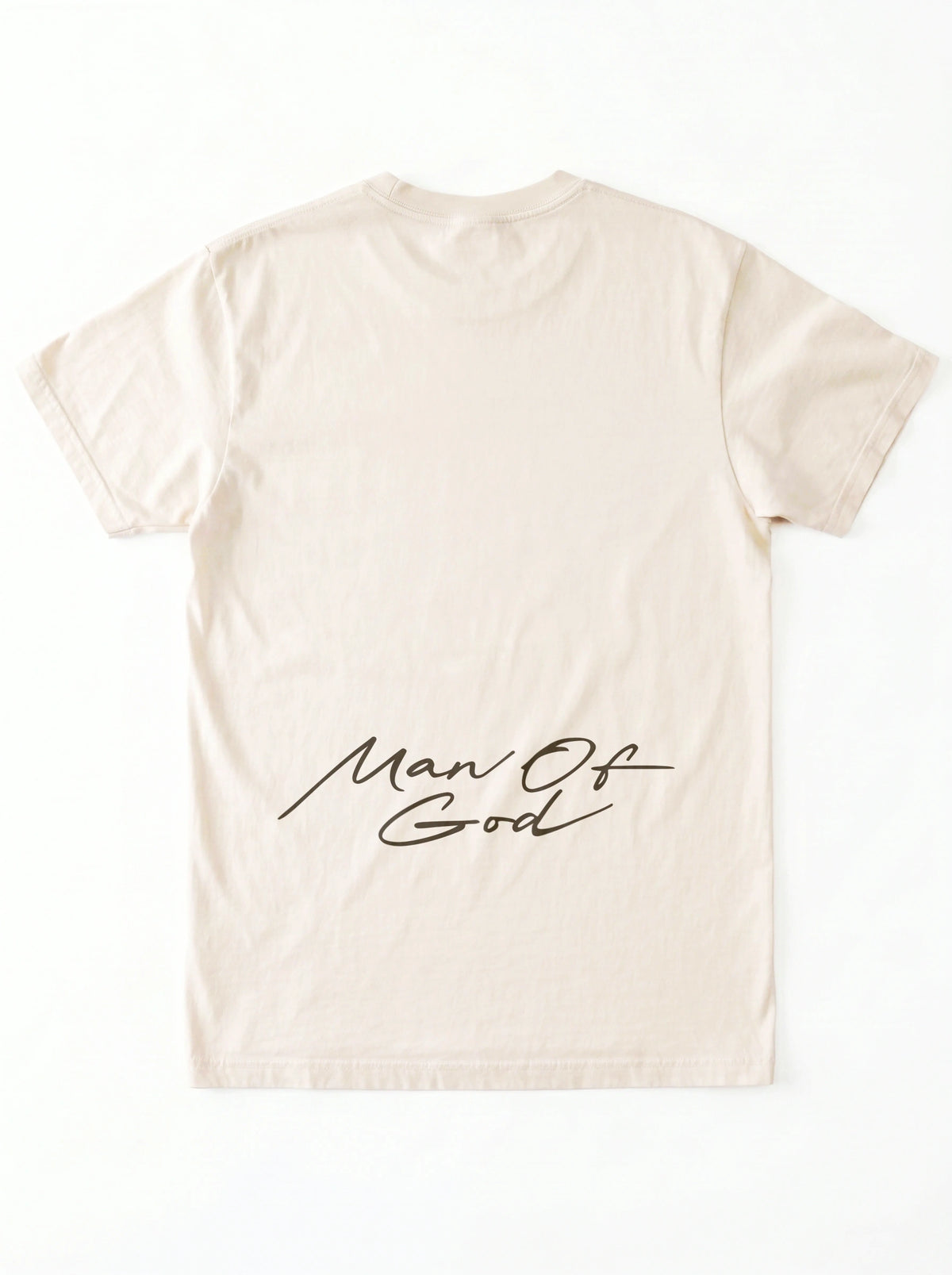 Back of a cream T-shirt laid flat with a large black script graphic across the lower back reading “Man Of God.”